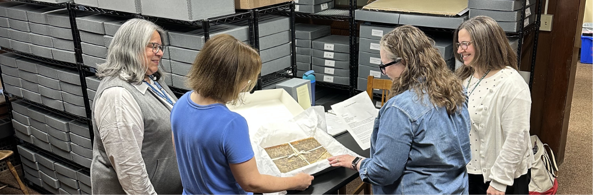 A group of four people reviews a document in an archives collection storage room.