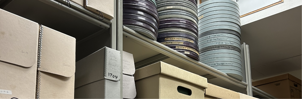 A cropped view of a metal storage shelf with record cartons on one shelf and metal film canisters stacked on another.
